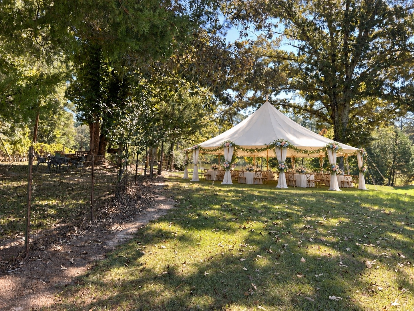 White reception tent dressed with greenery and flowers beneath the trees